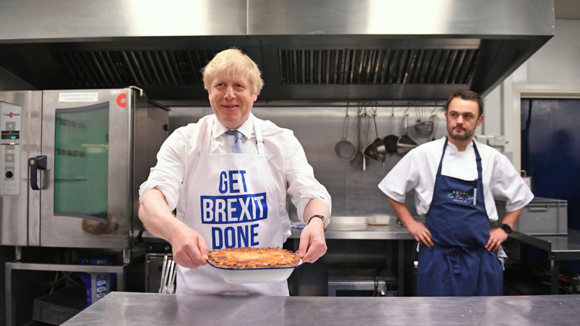 Prime Minister Boris Johnson holds a freshly baked pie while wearing a 'get Brexit done' apron. - Credit: Stefan Rousseau/PA.