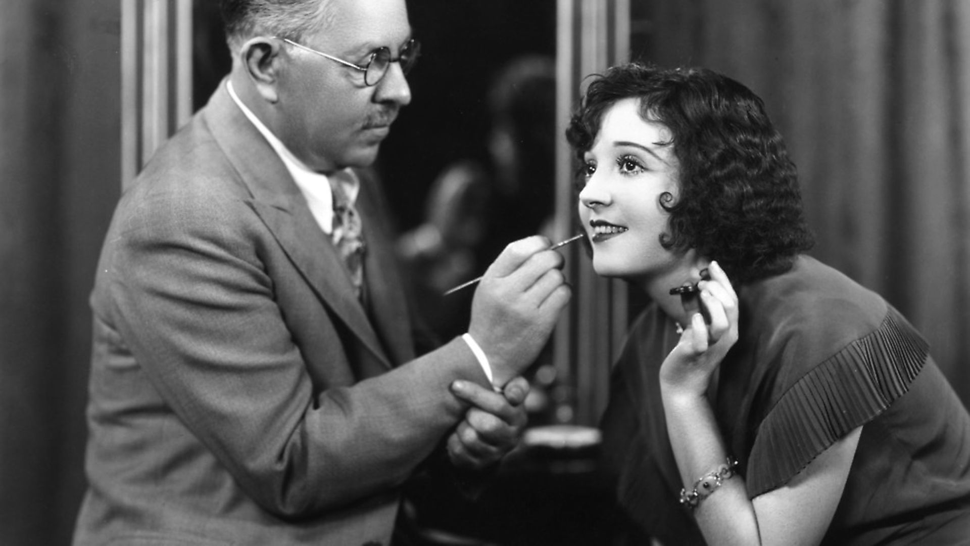 Max Factor, Polish businessman and founder of cosmetics company, Max Factor, demonstrates the technique of applying lipstick on US silent film actress Madge Bellamy. Photo: Margaret Chute/Hulton Archive/Getty Images - Credit: Getty Images