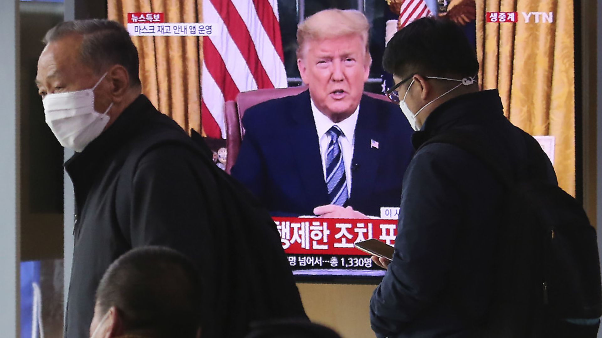 Masked people walk in front of a TV screen showing a live broadcast of U.S. President Donald Trump's speech at the Seoul Railway Station in Seoul, South Korea. (AP Photo/Ahn Young-joon) - Credit: AP