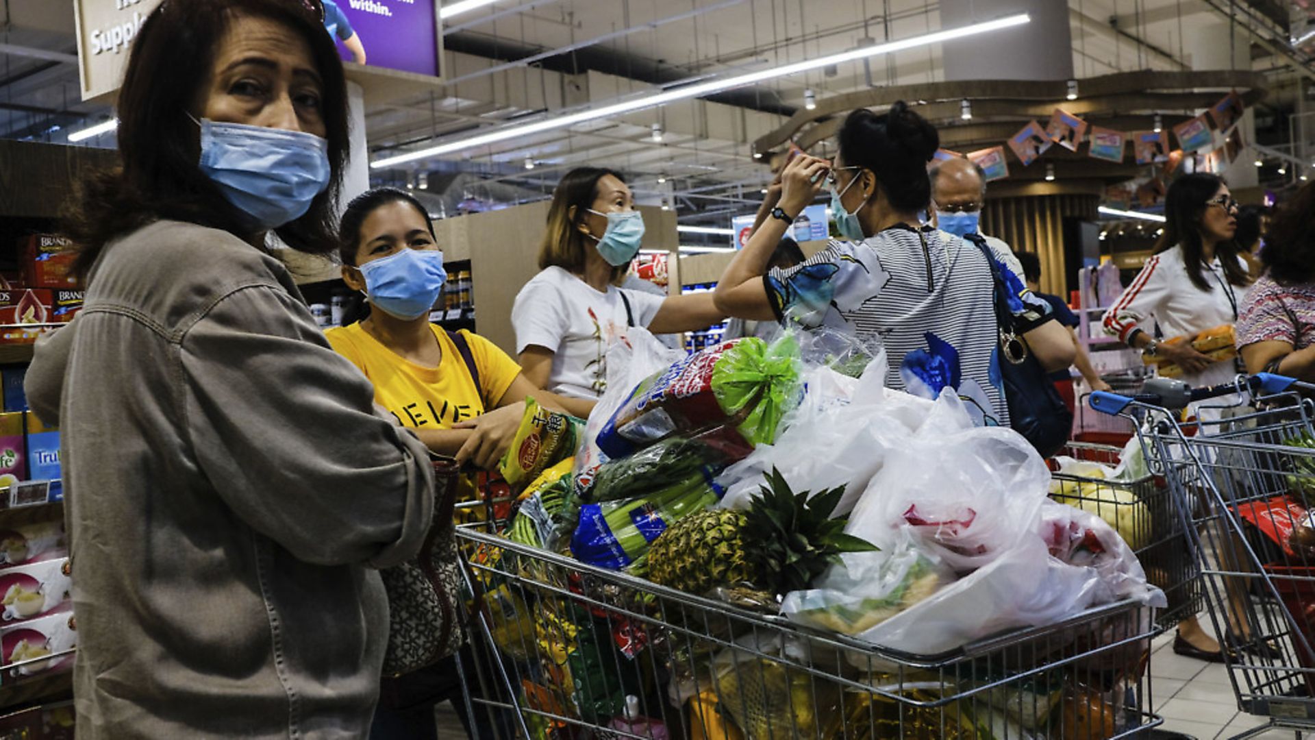 Shoppers wearing face masks with a cart full of food supplies wait in line to pay at a supermarket counter in Singapore. (AP Photo/Ee Ming Toh) - Credit: AP