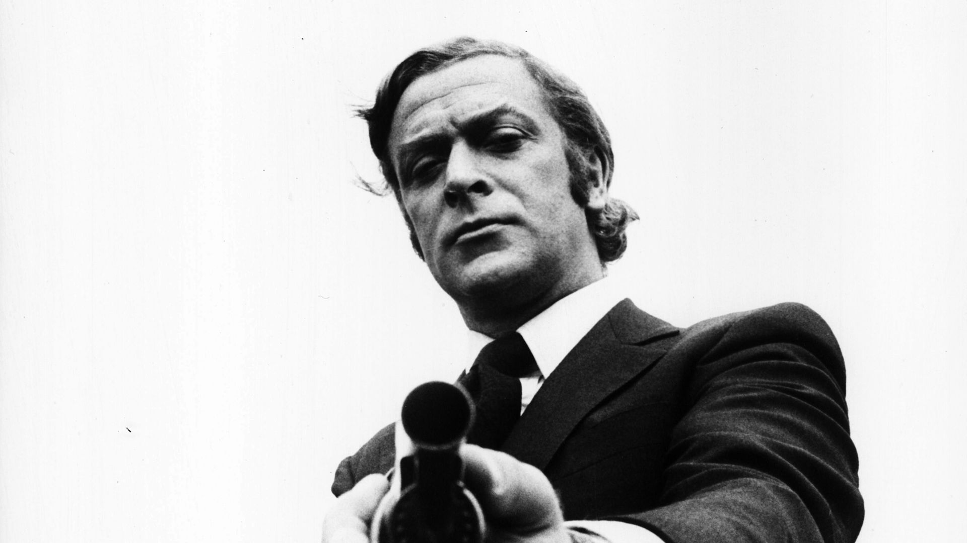 Portrait of actor Michael Caine pointing a gun towards the camera, as he appears in the film 'Get Carter', 1971. (Photo by Stanley Bielecki Movie Collection/Getty Images) - Credit: Getty Images