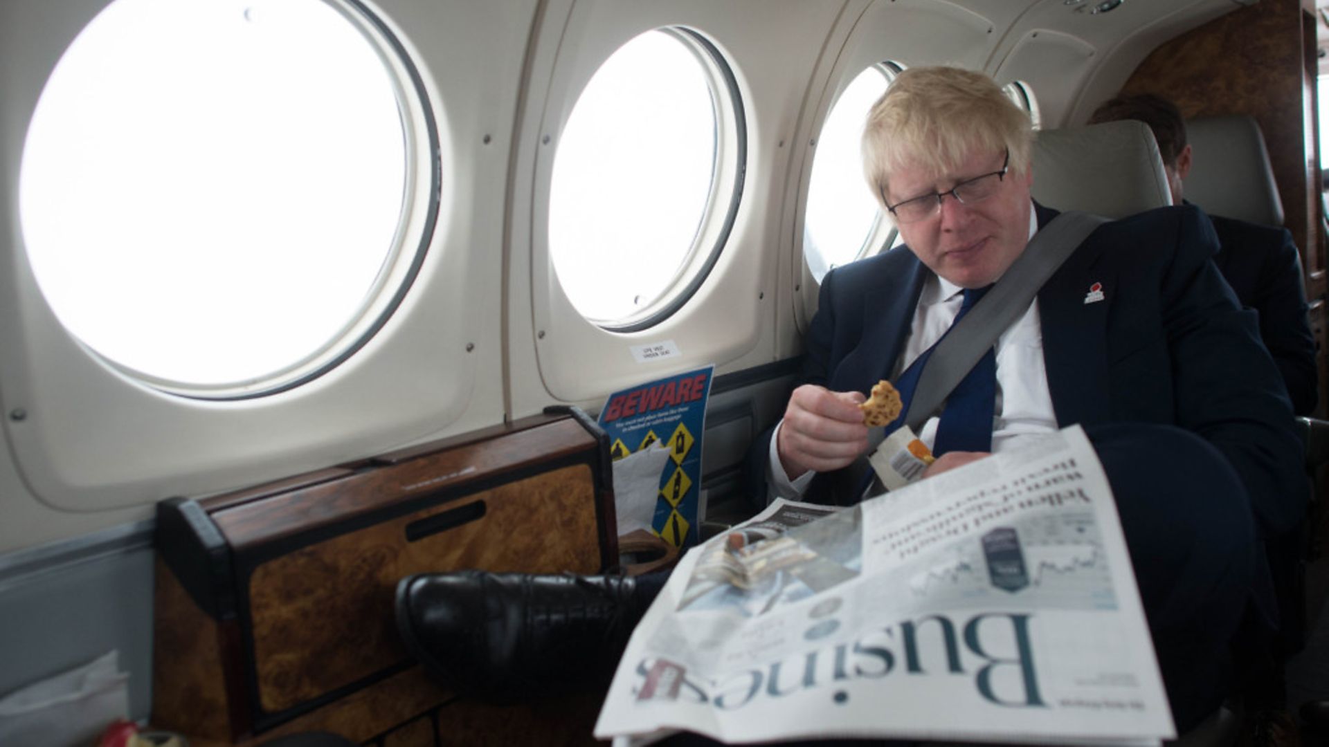 Boris Johnson reads a newspaper on a plane - Credit: Stefan Rousseau/PA