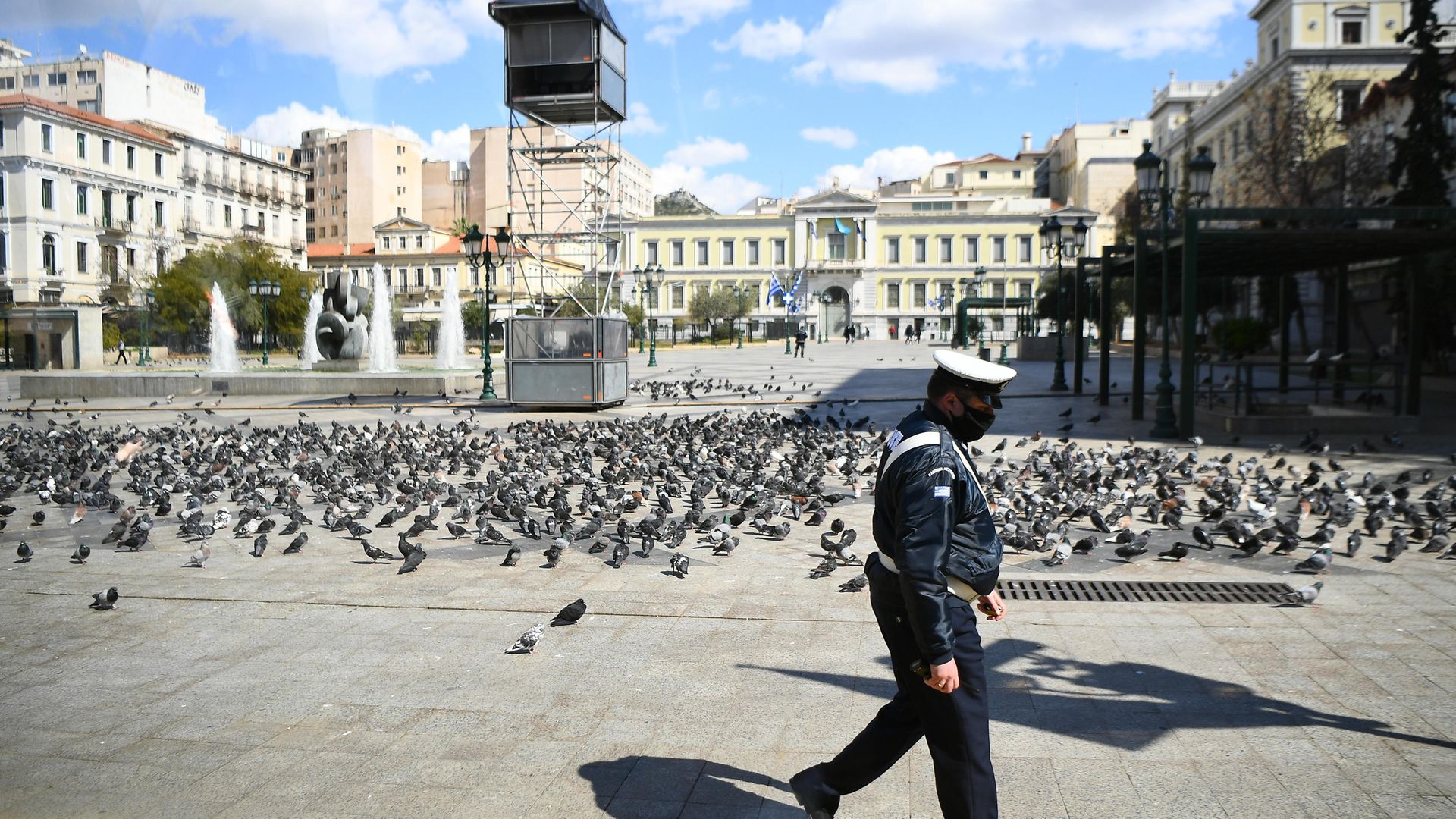 A police officer walks past an empty square in the centre of Athens, Greece, during lockdown - Credit: PA