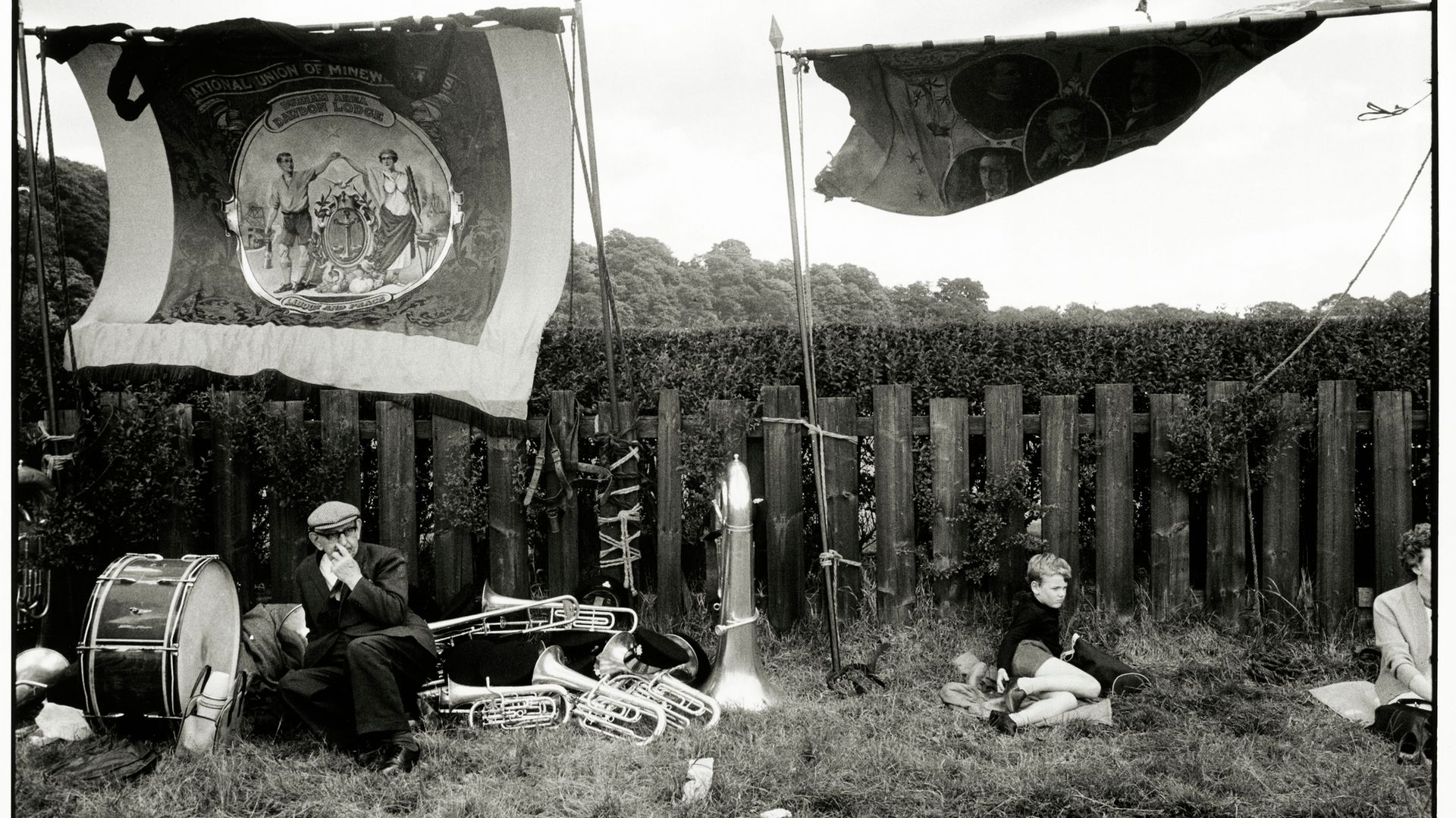 Trade union banners fly as people rest amid musical instruments during the 1969 Durham Miners' Gala, a major union gathering. The image was taken by Tony Ray-Jones, a photographer known for capturing the unguarded moments of people from all sections of British society - Credit: SSPL via Getty Images