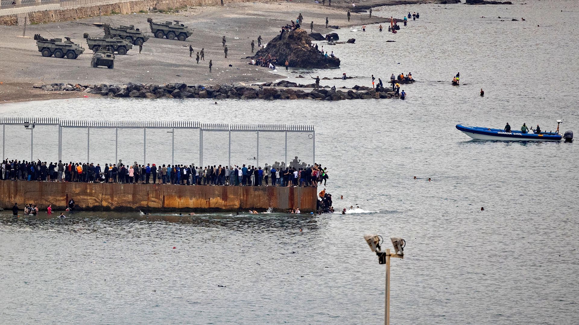 Migrants rally by a border fence to cross from Morocco to Spain's North African enclave of Ceuta, where Spanish troops await - Credit: AFP via Getty Images