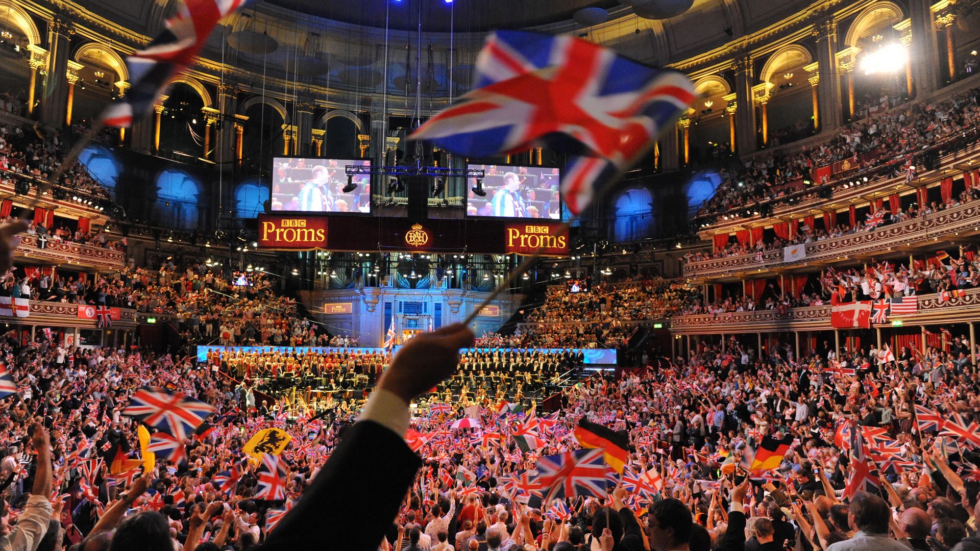 Union flags (and those of other nations) are waved during the climax of Last Night of the Proms - Credit: Redferns via Getty Images