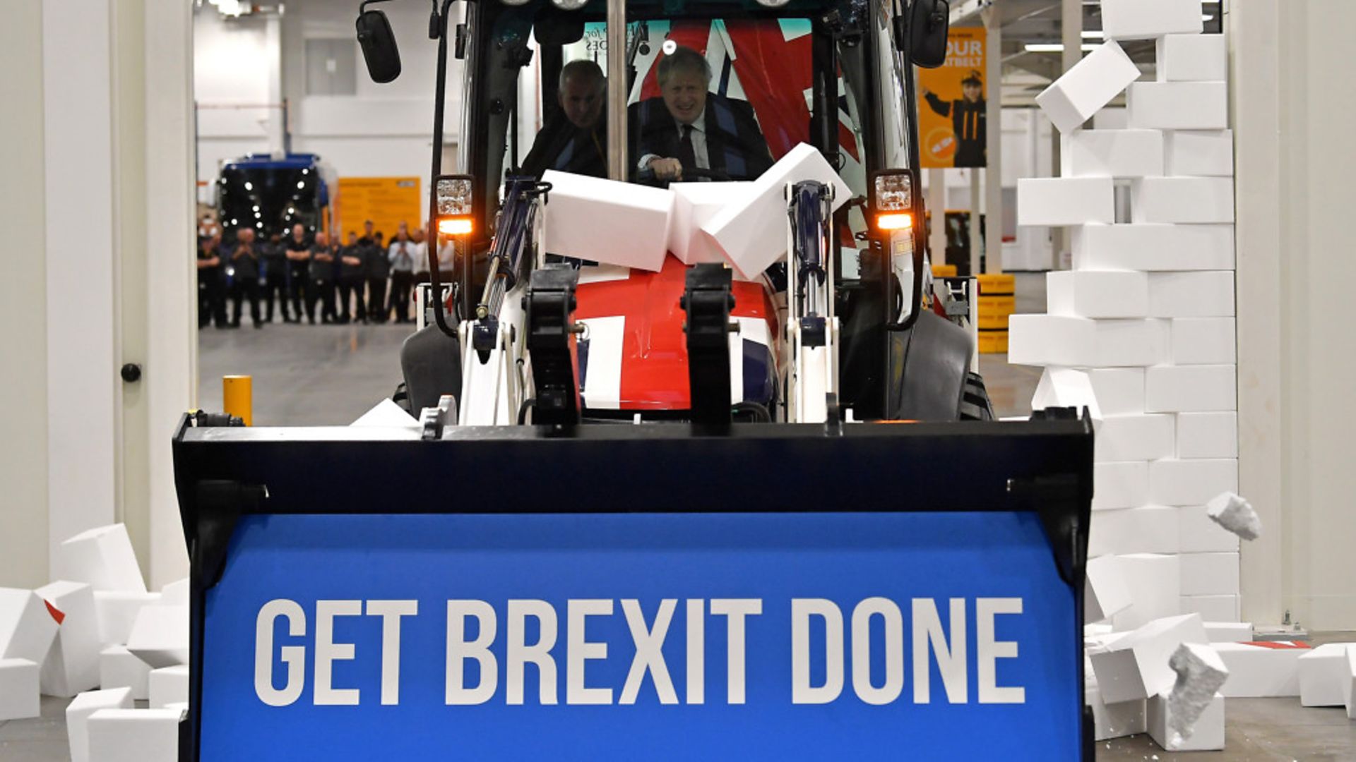 Boris Johnson drives a union flag-themed JCB, with the words "Get Brexit Done" inside the digger bucket, through a fake wall - Credit: Getty Images