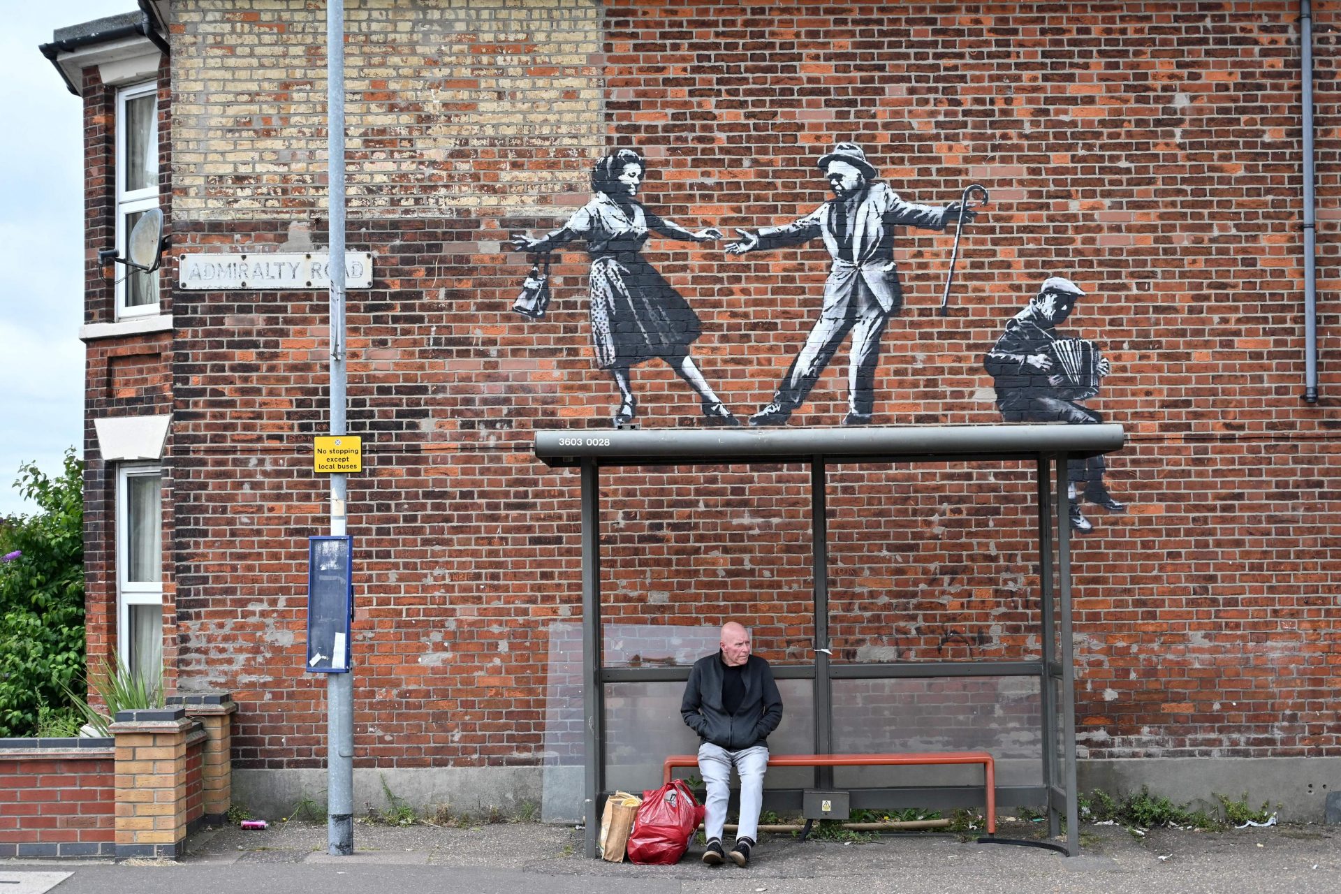 A man and his shopping at a bus stop in Great Yarmouth, below Banksy’s graffiti artwork of a couple dancing to an accordion player. Photo: Justin Tallis/AFP via Getty Images.