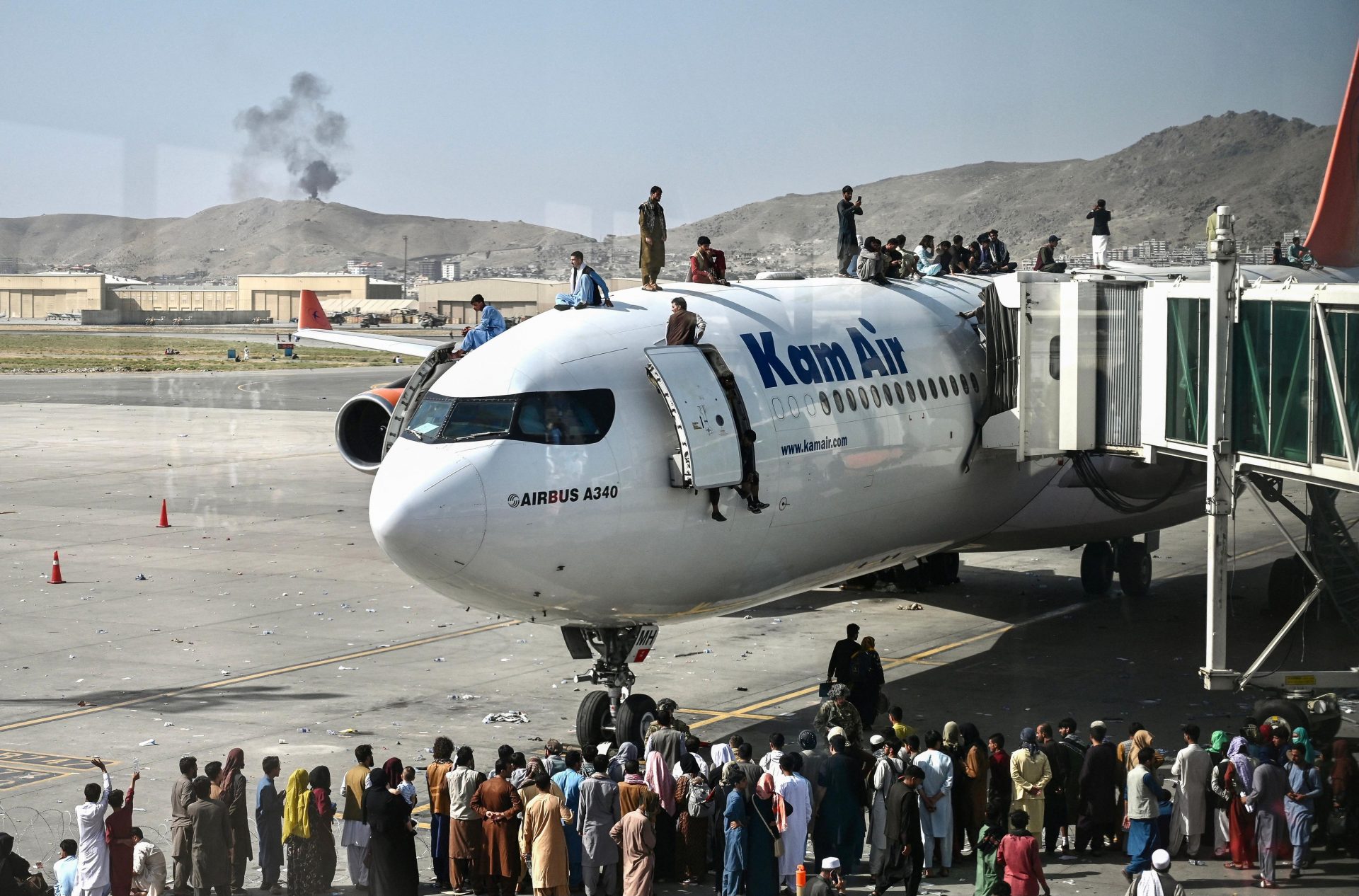 Afghan people climb atop a plane as they wait at the Kabul airport. (Photo by Wakil Kohsar / AFP) 